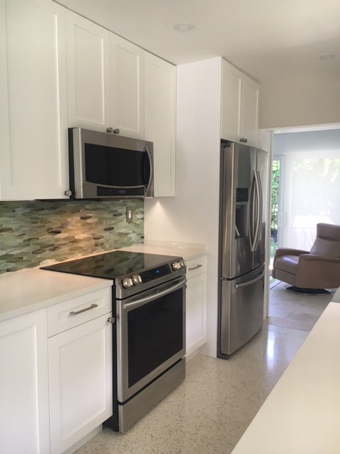 Inspiration for a mid-sized coastal l-shaped beige floor and terrazzo floor open concept kitchen remodel in Miami with a farmhouse sink, shaker cabinets, white cabinets, quartz countertops, glass tile backsplash, stainless steel appliances, no island, green backsplash and white countertops