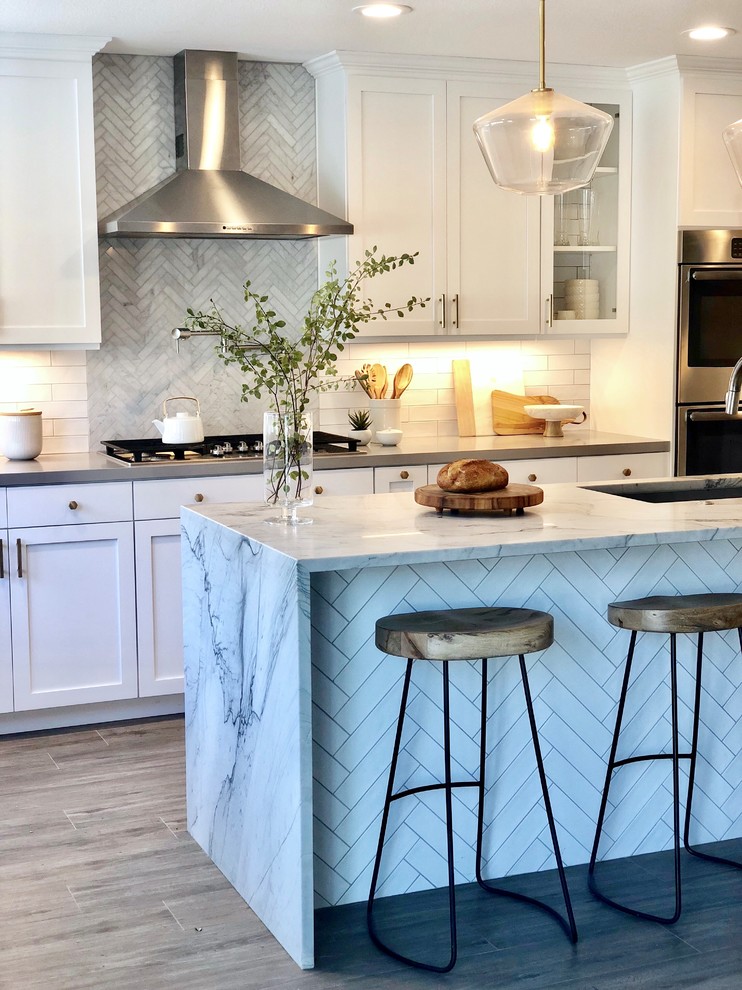 Bild på ett mellanstort vintage grå grått kök, med en undermonterad diskho, skåp i shakerstil, vita skåp, marmorbänkskiva, vitt stänkskydd, stänkskydd i tunnelbanekakel, rostfria vitvaror, mellanmörkt trägolv, en köksö och brunt golv