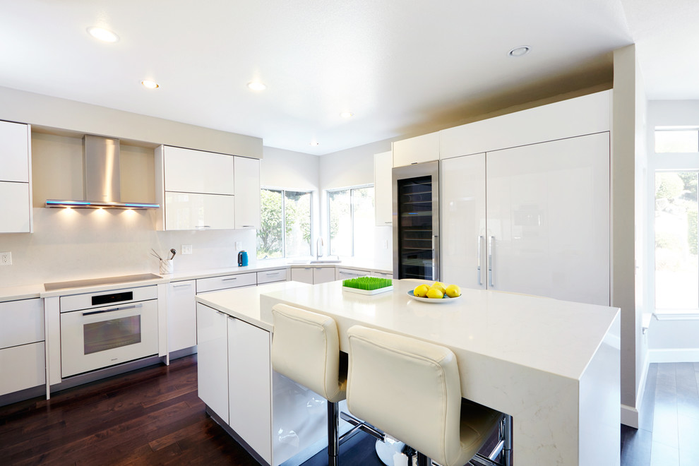 Immagine di una grande cucina minimal con lavello da incasso, ante lisce, ante bianche, top in granito, paraspruzzi bianco, elettrodomestici bianchi e parquet scuro