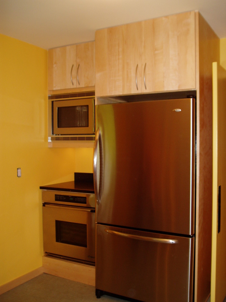他の地域にあるコンテンポラリースタイルのおしゃれなキッチン (フラットパネル扉のキャビネット、淡色木目調キャビネット、クオーツストーンカウンター、黒いキッチンパネル、シルバーの調理設備) の写真