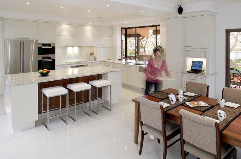 Eat-in kitchen - u-shaped ceramic tile eat-in kitchen idea in Sydney with a drop-in sink, flat-panel cabinets, white cabinets, solid surface countertops, white backsplash, glass sheet backsplash, stainless steel appliances and an island
