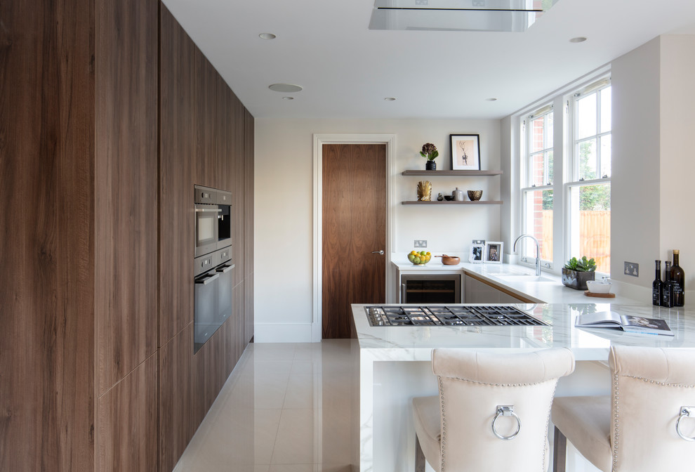 Example of a large trendy u-shaped ceramic tile, beige floor and tray ceiling open concept kitchen design in London with flat-panel cabinets, dark wood cabinets, a peninsula, white countertops, solid surface countertops and a drop-in sink