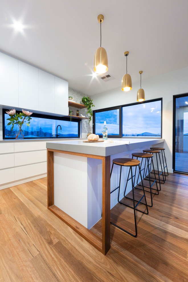 Example of a mid-sized minimalist medium tone wood floor open concept kitchen design in Canberra - Queanbeyan with an undermount sink, white cabinets, quartz countertops, white backsplash, subway tile backsplash, black appliances, two islands and gray countertops