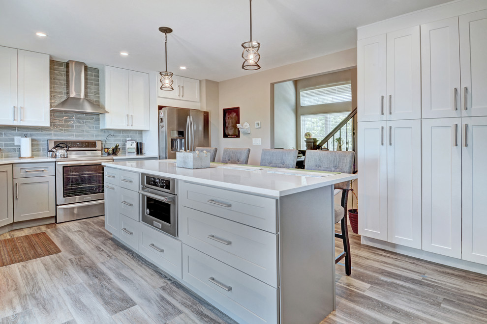 Mid-sized transitional l-shaped vinyl floor and multicolored floor eat-in kitchen photo in Other with shaker cabinets, yellow cabinets, quartz countertops, gray backsplash, ceramic backsplash, stainless steel appliances, an island and white countertops