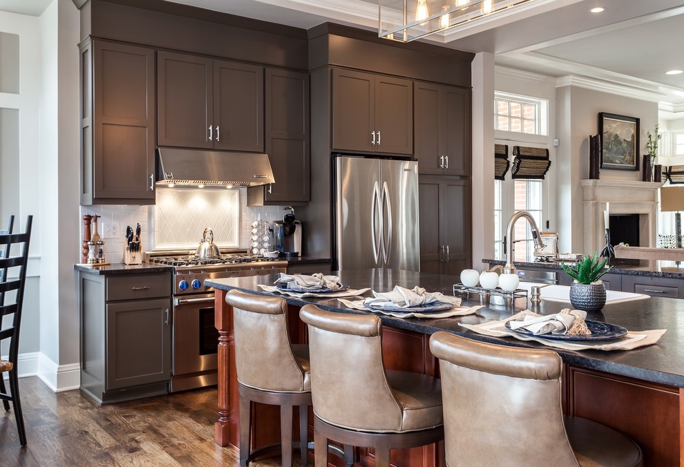 Mid-sized transitional single-wall medium tone wood floor open concept kitchen photo in Denver with a farmhouse sink, shaker cabinets, gray cabinets, quartz countertops, white backsplash, ceramic backsplash, stainless steel appliances and two islands