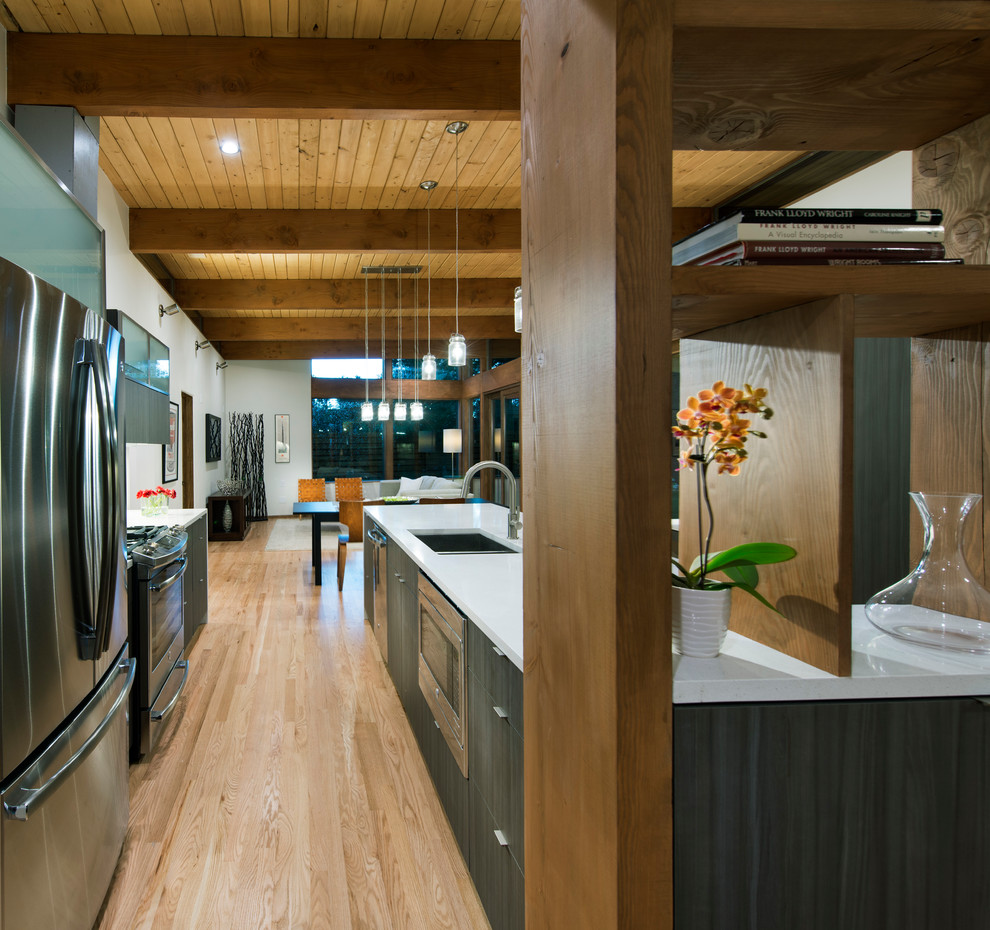 Retro galley open plan kitchen in Denver with a submerged sink, flat-panel cabinets, dark wood cabinets, engineered stone countertops, white splashback, glass tiled splashback, stainless steel appliances, light hardwood flooring and an island.