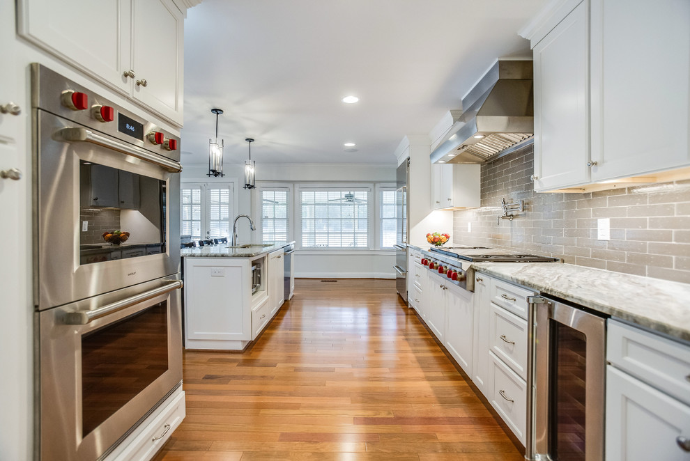 Inredning av ett klassiskt mellanstort flerfärgad flerfärgat kök, med en dubbel diskho, luckor med infälld panel, vita skåp, marmorbänkskiva, grått stänkskydd, stänkskydd i keramik, rostfria vitvaror, mellanmörkt trägolv, en köksö och rött golv