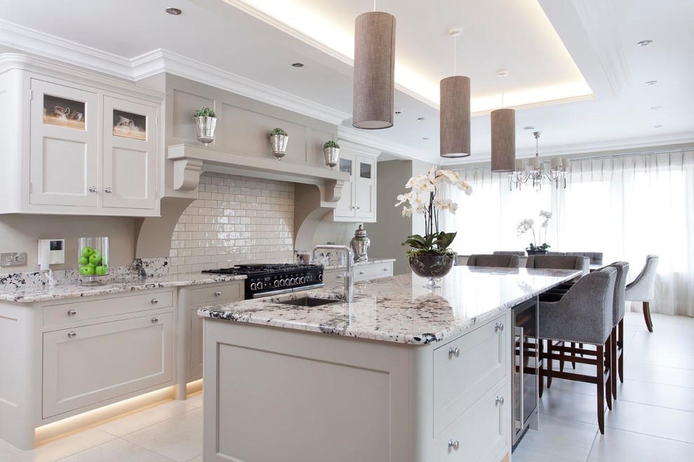 Large traditional open plan kitchen in Other with beaded cabinets, grey cabinets, granite worktops, beige splashback, metro tiled splashback, ceramic flooring, an island, black appliances and a submerged sink.