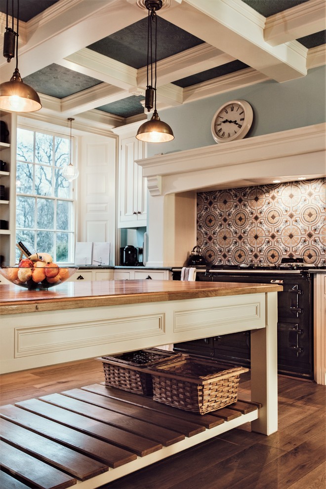 Klassische Küche mit schwarzen Elektrogeräten, dunklem Holzboden, Kücheninsel, braunem Boden und bunter Rückwand in Sonstige