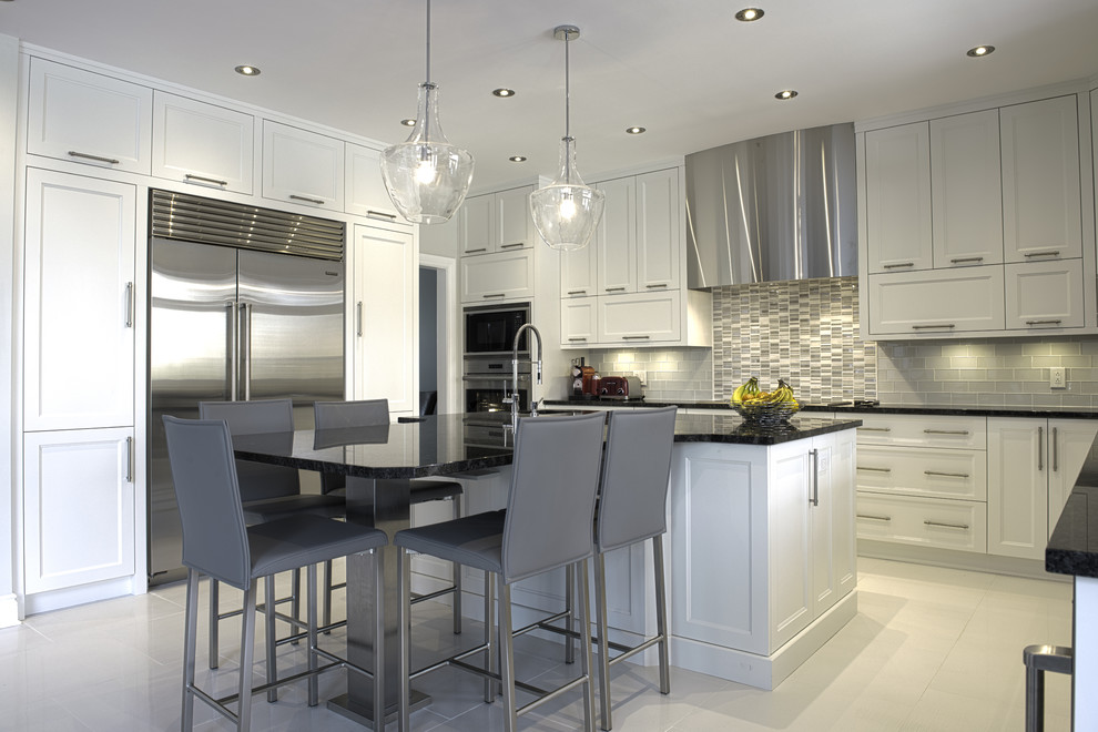Large contemporary u-shaped kitchen/diner in Montreal with a submerged sink, shaker cabinets, white cabinets, granite worktops, white splashback, glass tiled splashback, stainless steel appliances, ceramic flooring, an island, beige floors and black worktops.