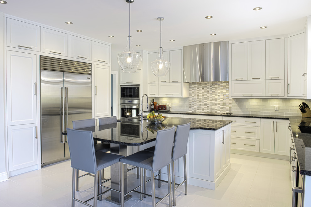 Large contemporary u-shaped kitchen/diner in Montreal with a submerged sink, shaker cabinets, white cabinets, granite worktops, white splashback, glass tiled splashback, stainless steel appliances, ceramic flooring, an island, beige floors and black worktops.