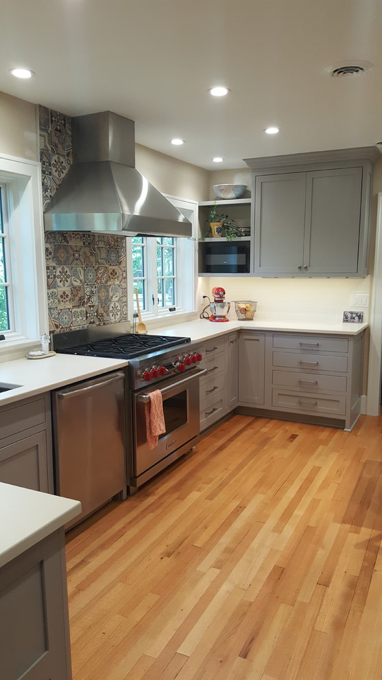 Medium sized traditional u-shaped kitchen in Other with shaker cabinets, grey cabinets, composite countertops, white splashback, metro tiled splashback, stainless steel appliances and light hardwood flooring.