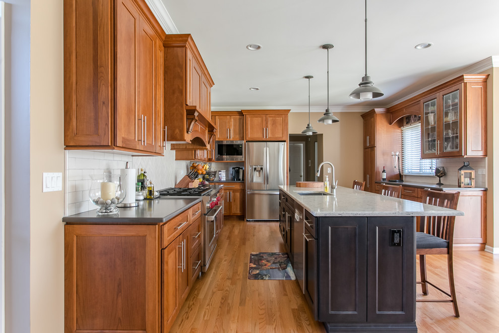 Example of a mid-sized classic u-shaped medium tone wood floor and brown floor eat-in kitchen design in Chicago with an undermount sink, shaker cabinets, medium tone wood cabinets, quartz countertops, white backsplash, subway tile backsplash, stainless steel appliances, an island and multicolored countertops