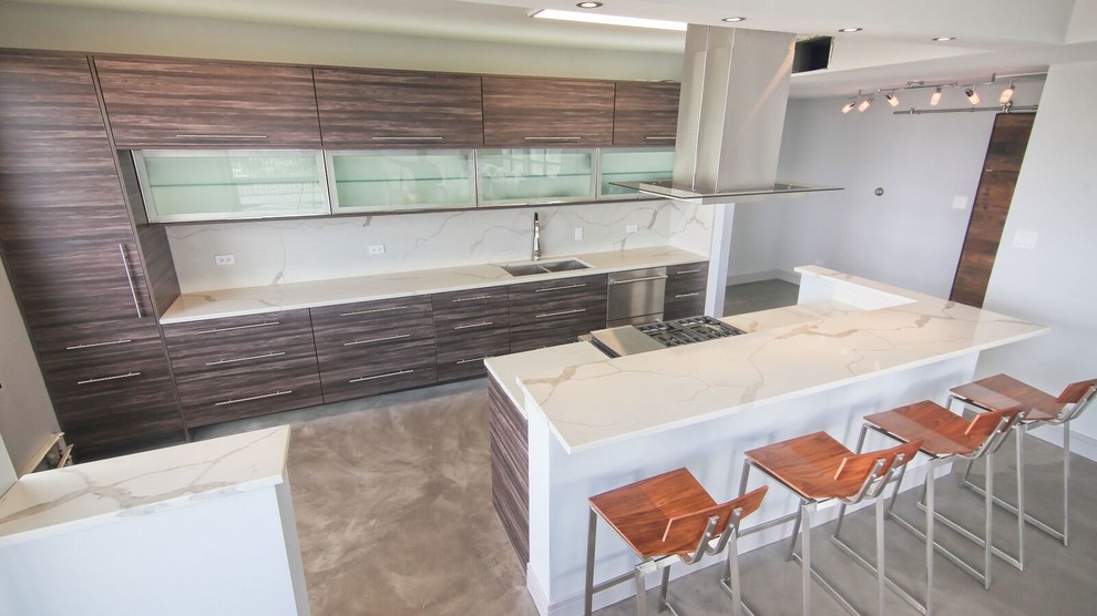 Foto på ett mellanstort industriellt kök, med en undermonterad diskho, släta luckor, grå skåp, bänkskiva i kvartsit, vitt stänkskydd, betonggolv, en köksö och grått golv
