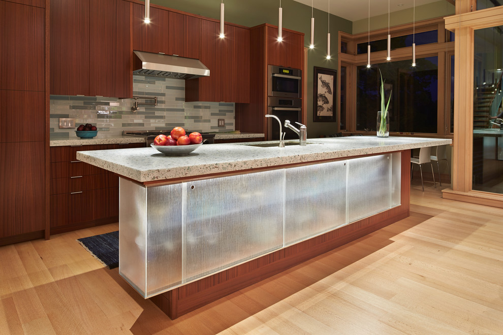 Example of a mid-sized minimalist galley light wood floor open concept kitchen design in Seattle with an undermount sink, flat-panel cabinets, medium tone wood cabinets, recycled glass countertops, gray backsplash, glass tile backsplash, stainless steel appliances and an island