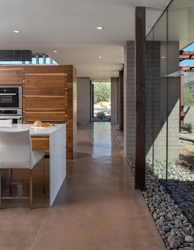 Moderne Küche mit flächenbündigen Schrankfronten, hellbraunen Holzschränken, Küchengeräten aus Edelstahl, Betonboden und Kücheninsel in Phoenix
