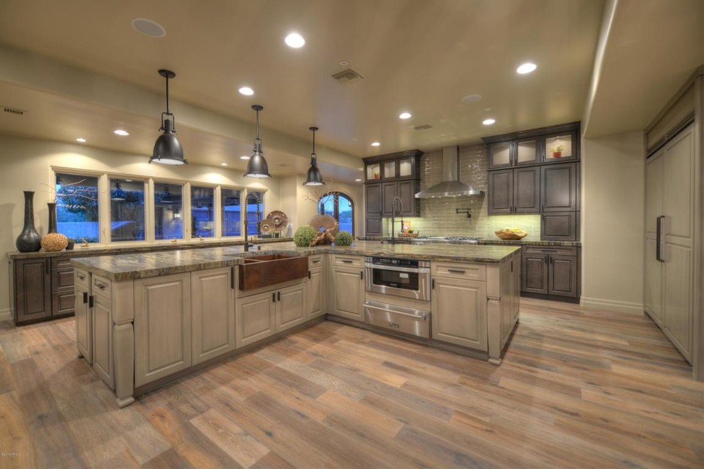 Large transitional l-shaped medium tone wood floor eat-in kitchen photo in Phoenix with a farmhouse sink, raised-panel cabinets, gray cabinets, granite countertops, beige backsplash, ceramic backsplash, paneled appliances and an island