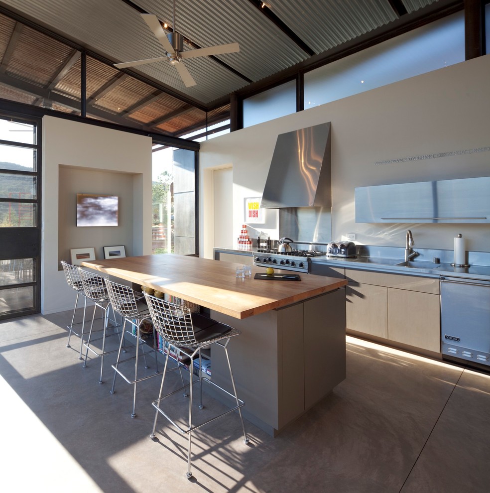 Inspiration for a contemporary galley kitchen in Albuquerque with an integrated sink, flat-panel cabinets, stainless steel cabinets, stainless steel worktops, stainless steel appliances, concrete flooring and an island.