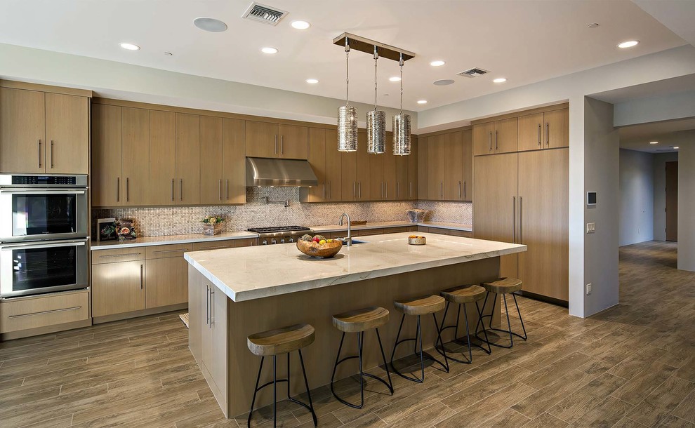 Moderne Küche in L-Form mit flächenbündigen Schrankfronten, hellbraunen Holzschränken, bunter Rückwand, Elektrogeräten mit Frontblende und Kücheninsel in Sonstige