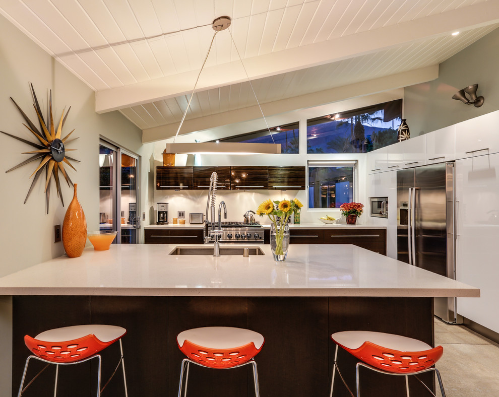 ロサンゼルスにあるミッドセンチュリースタイルのおしゃれなキッチン (アンダーカウンターシンク、フラットパネル扉のキャビネット、濃色木目調キャビネット、白いキッチンパネル、シルバーの調理設備) の写真