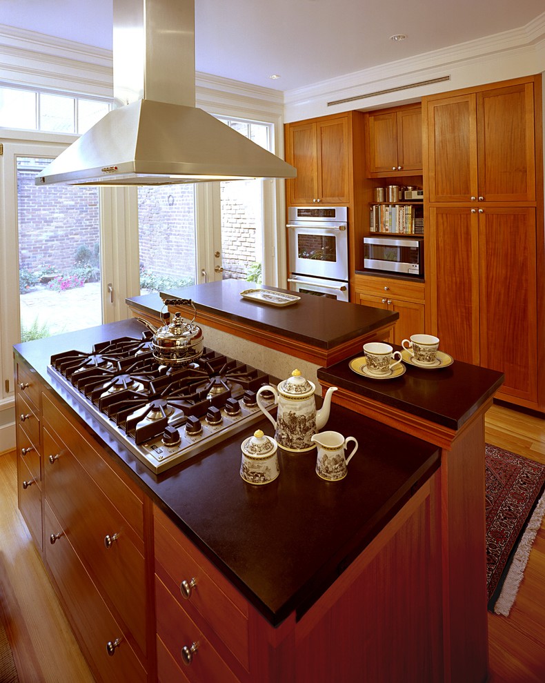 Cette image montre une cuisine américaine traditionnelle en bois brun avec un placard à porte shaker, un plan de travail en quartz modifié et un électroménager en acier inoxydable.