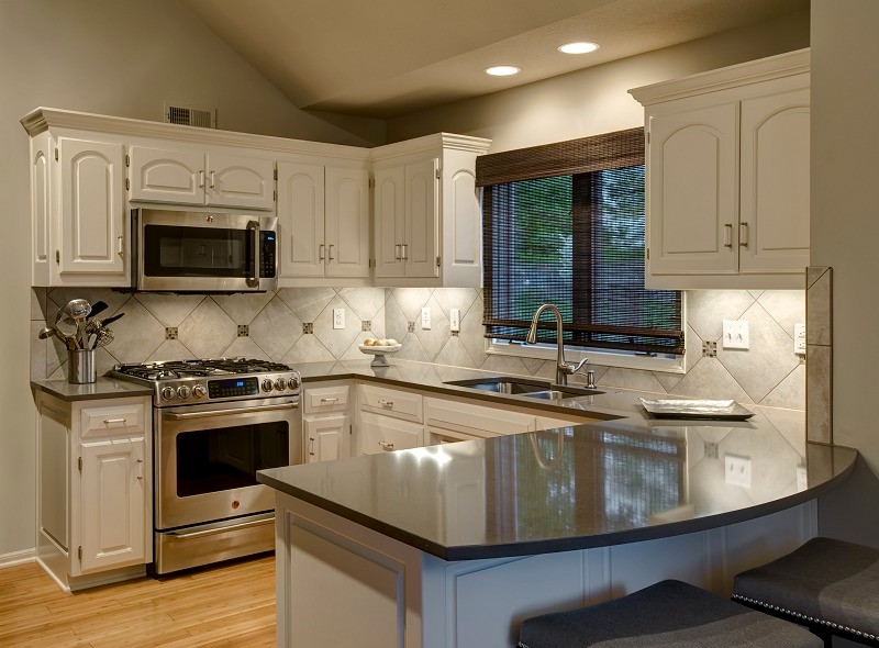 Exempel på ett litet klassiskt kök, med en dubbel diskho, luckor med profilerade fronter, vita skåp, bänkskiva i kvarts, grått stänkskydd, stänkskydd i stenkakel, rostfria vitvaror, ljust trägolv och en halv köksö