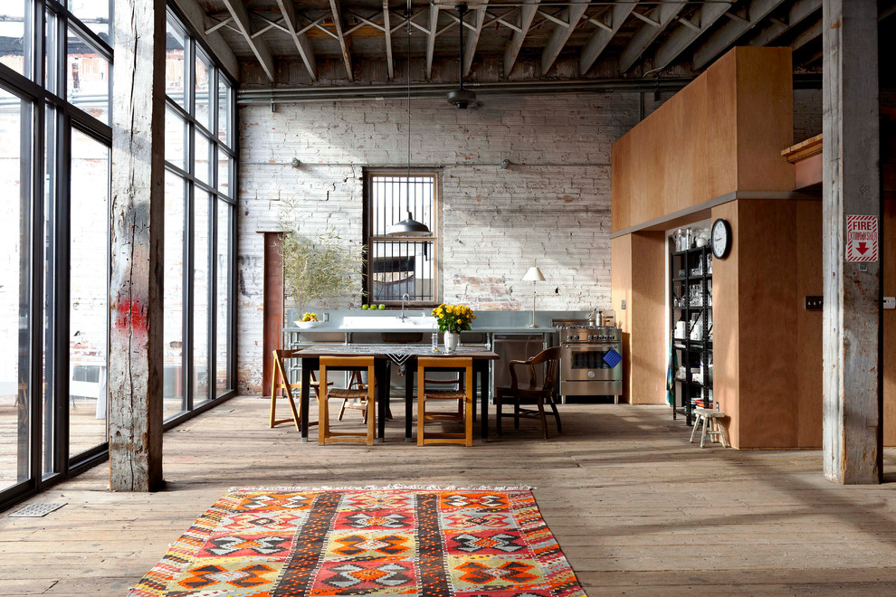 Zweizeilige Industrial Wohnküche mit Küchengeräten aus Edelstahl und braunem Holzboden in Sonstige