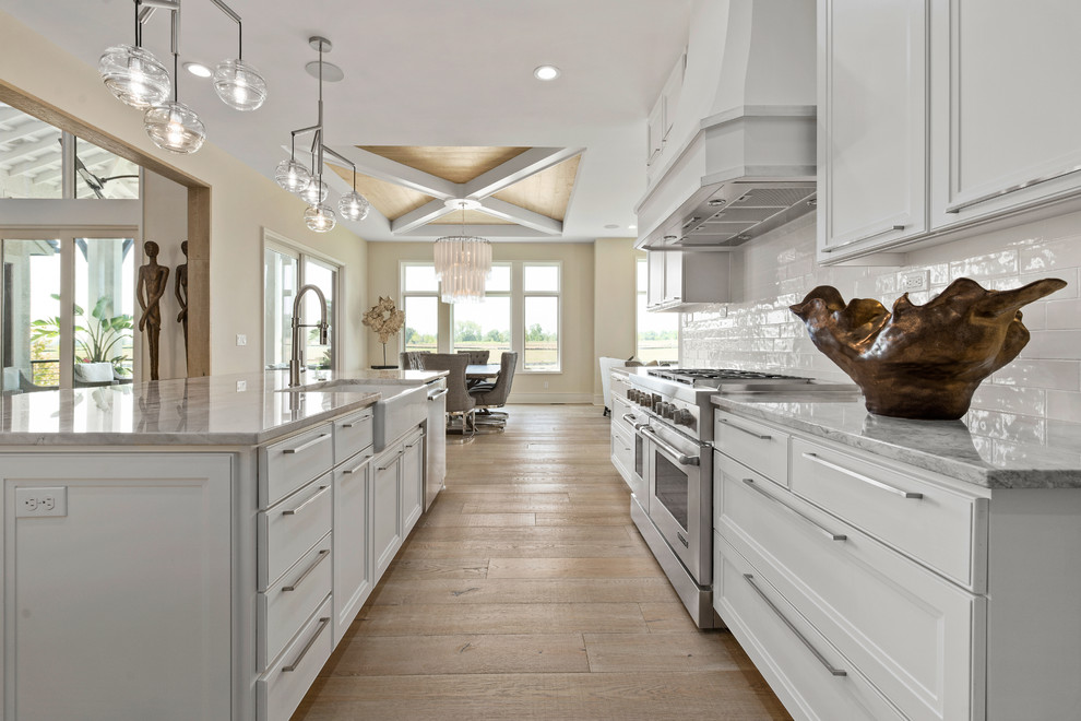 Klassisk inredning av ett mellanstort grå grått kök, med vita skåp, granitbänkskiva, vitt stänkskydd, stänkskydd i keramik, rostfria vitvaror, ljust trägolv, en köksö, en rustik diskho, luckor med infälld panel och beiget golv