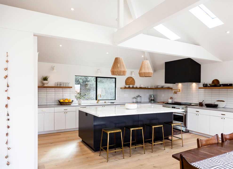 Photo of a contemporary l-shaped kitchen in Los Angeles with a submerged sink, flat-panel cabinets, white cabinets, white splashback, light hardwood flooring, an island, beige floors, grey worktops and a vaulted ceiling.