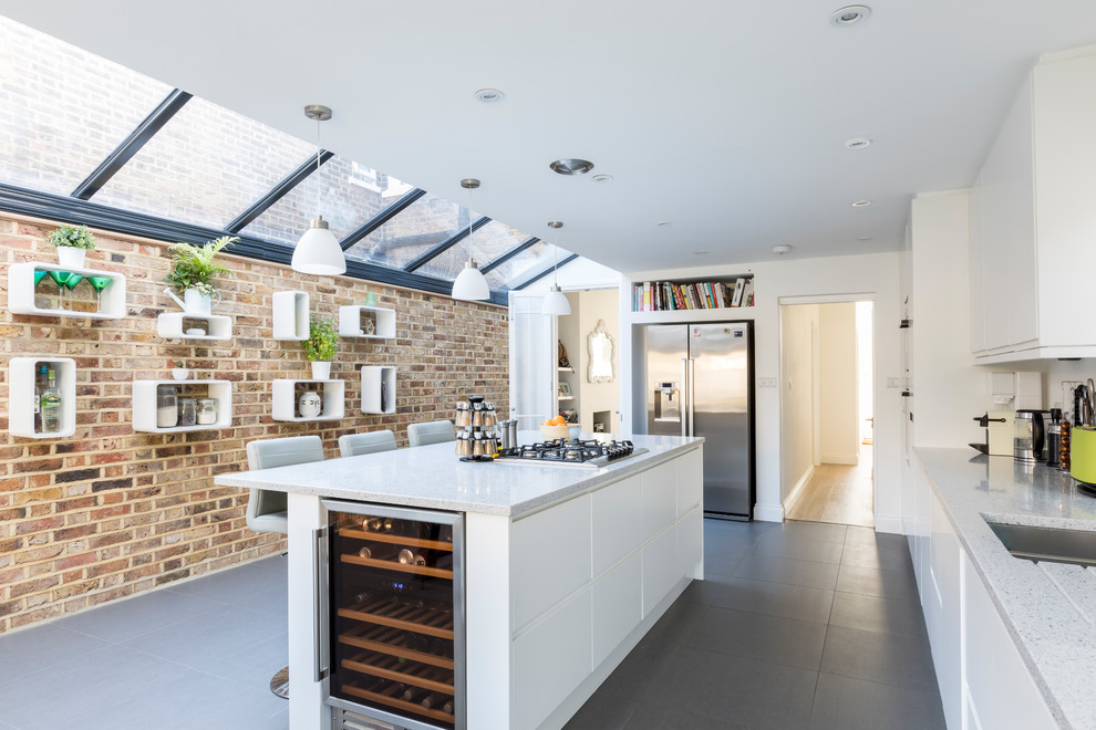 This is an example of a contemporary galley enclosed kitchen in London with a submerged sink, flat-panel cabinets, white cabinets, stainless steel appliances, an island and grey floors.
