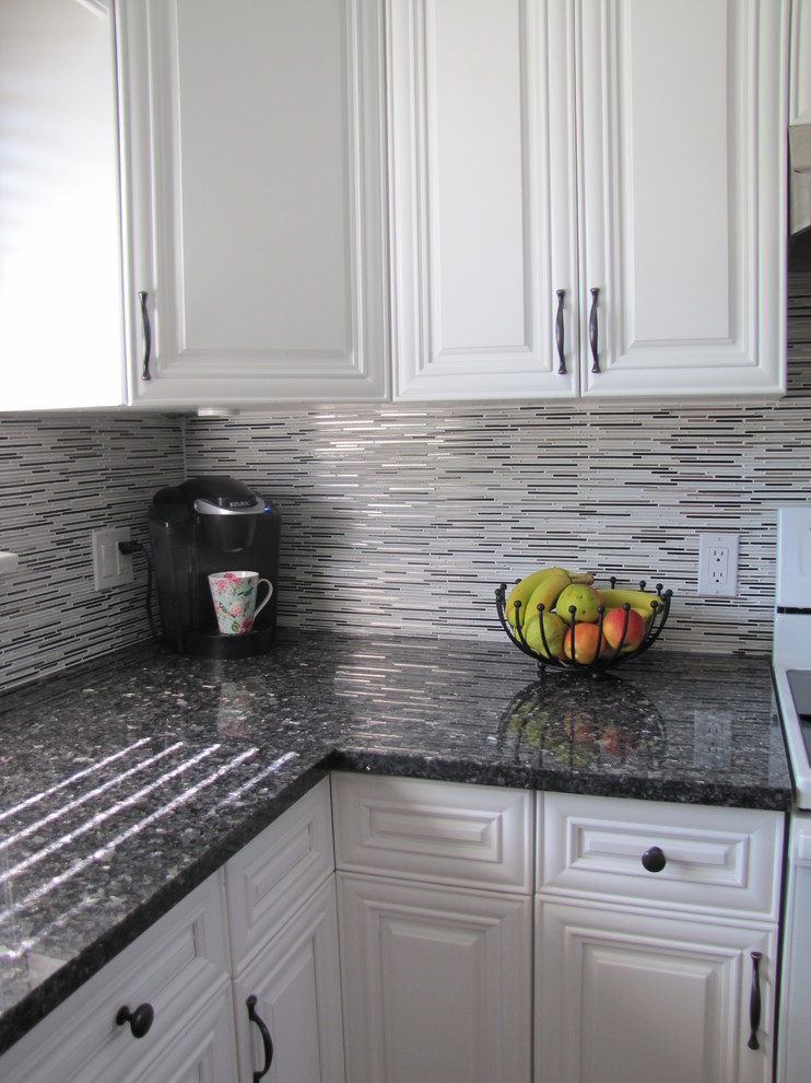 Inredning av ett modernt u-kök, med en undermonterad diskho, granitbänkskiva, stänkskydd med metallisk yta, stänkskydd i glaskakel och vita vitvaror