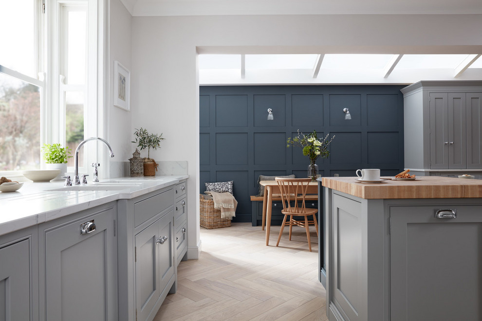 Large classic l-shaped open plan kitchen in London with shaker cabinets, grey cabinets, granite worktops, white splashback, light hardwood flooring, an island and brown floors.