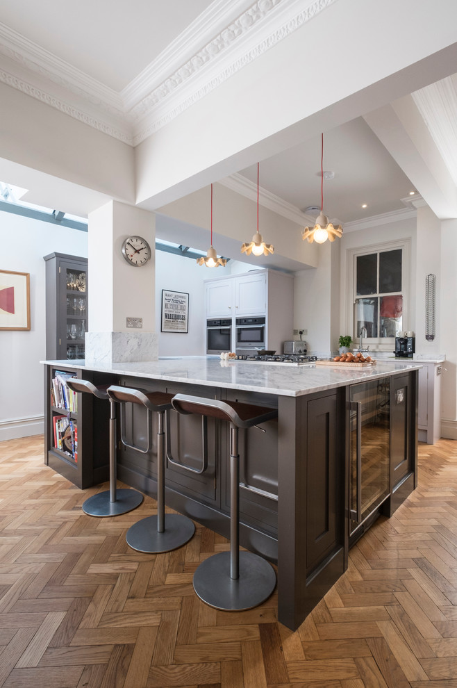This is an example of a traditional l-shaped open plan kitchen in Cardiff with a submerged sink, shaker cabinets, brown cabinets, marble worktops, stainless steel appliances, medium hardwood flooring and an island.