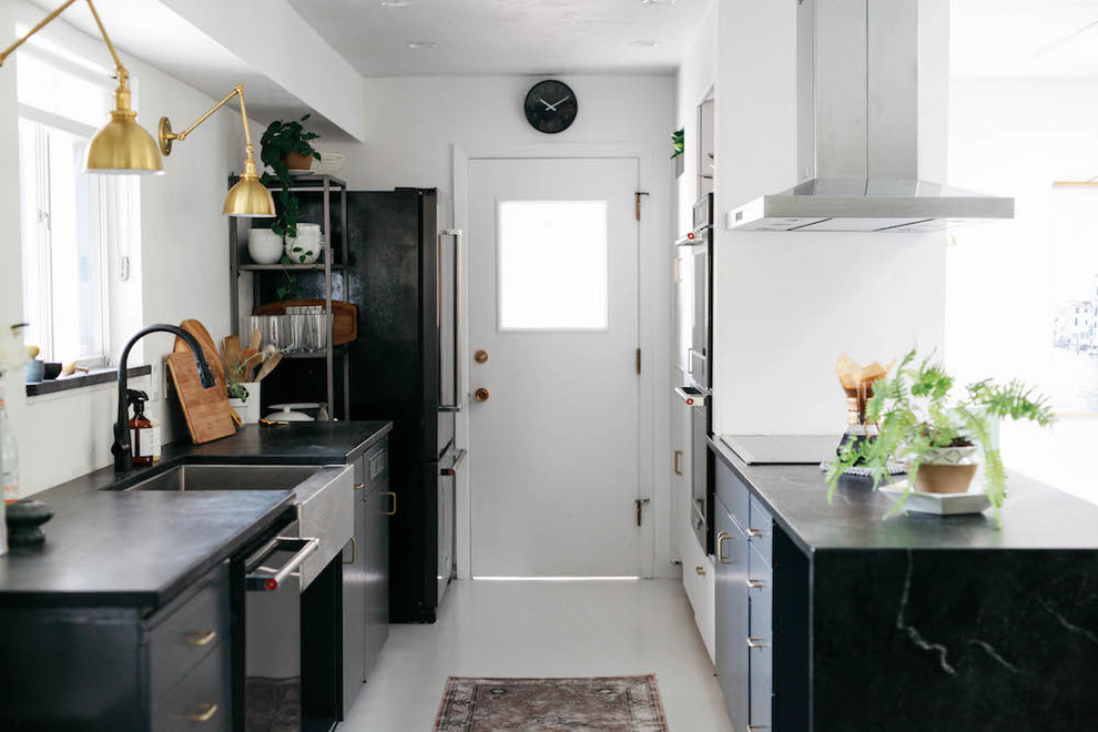 Foto de cocina comedor escandinava de tamaño medio con fregadero sobremueble, armarios con paneles lisos, puertas de armario grises, encimera de esteatita, salpicadero blanco, salpicadero de vidrio, electrodomésticos negros, suelo de madera pintada, península y suelo blanco