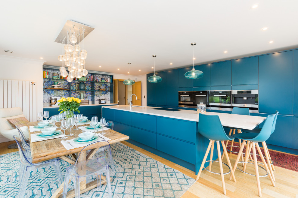Стильный дизайн: большая угловая кухня в современном стиле с обеденным столом, врезной мойкой, плоскими фасадами, белыми фасадами, разноцветным фартуком, техникой под мебельный фасад, островом, бежевым полом и синей столешницей - последний тренд