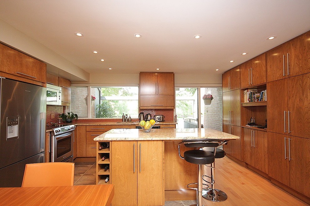 Inredning av ett modernt stort kök, med en undermonterad diskho, skåp i mellenmörkt trä, granitbänkskiva, orange stänkskydd, stänkskydd i glaskakel, rostfria vitvaror, ljust trägolv och en köksö