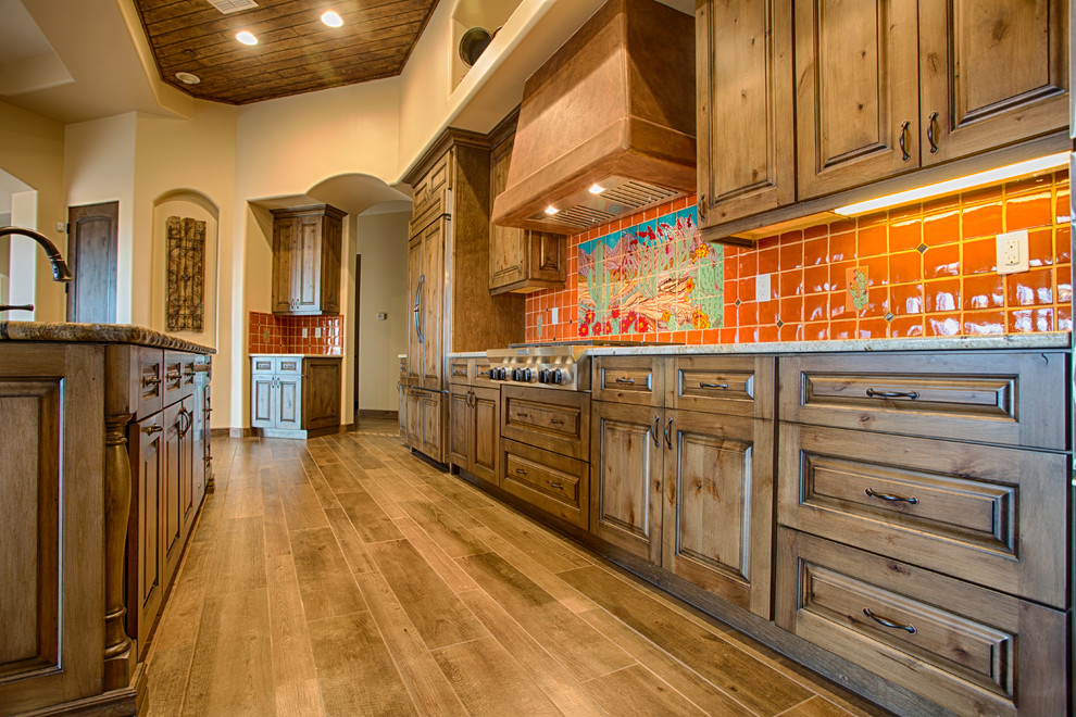 Exempel på ett stort amerikanskt linjärt kök och matrum, med en undermonterad diskho, luckor med upphöjd panel, skåp i mellenmörkt trä, granitbänkskiva, orange stänkskydd, stänkskydd i keramik, rostfria vitvaror, en köksö och mellanmörkt trägolv