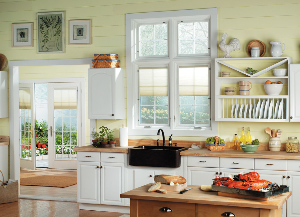 Bild på ett mellanstort vintage linjärt kök och matrum, med en rustik diskho, luckor med upphöjd panel, vita skåp, träbänkskiva, gult stänkskydd, stänkskydd i trä, svarta vitvaror, mellanmörkt trägolv, en köksö och brunt golv