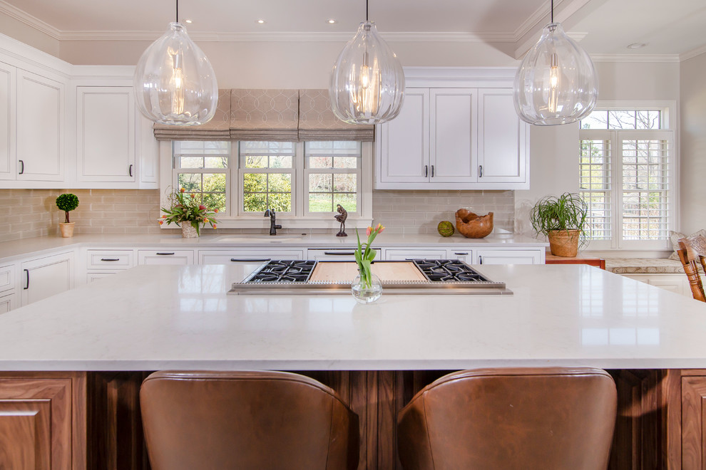Photo of a large traditional u-shaped kitchen/diner in Charlotte with beaded cabinets, white cabinets, composite countertops, beige splashback, glass tiled splashback, stainless steel appliances, ceramic flooring, an island, beige floors and grey worktops.