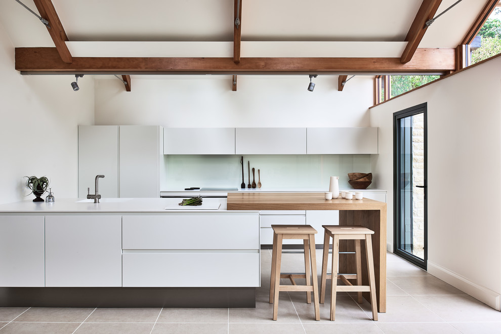 На фото: кухня в современном стиле с плоскими фасадами, белыми фасадами, белым фартуком, фартуком из стекла и полуостровом с