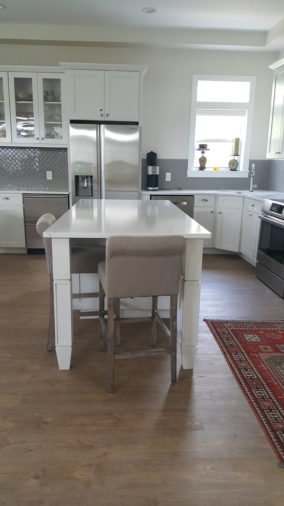 Example of a mid-sized transitional l-shaped medium tone wood floor eat-in kitchen design in Miami with an undermount sink, shaker cabinets, white cabinets, quartzite countertops, gray backsplash, glass sheet backsplash, stainless steel appliances and an island