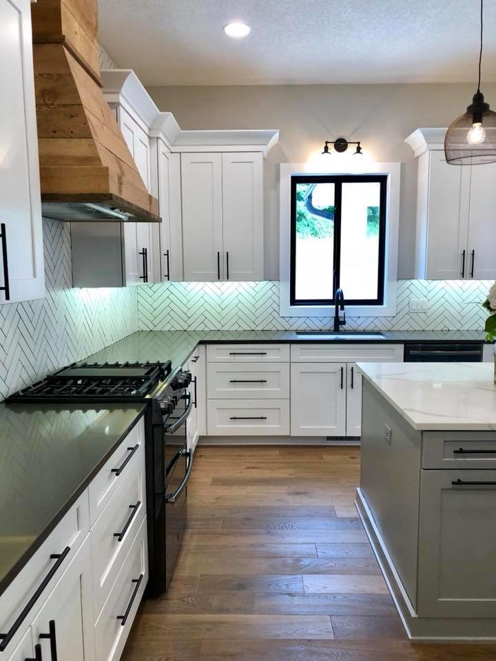 Inspiration for a mid-sized farmhouse u-shaped medium tone wood floor and brown floor open concept kitchen remodel in Other with an undermount sink, shaker cabinets, white cabinets, solid surface countertops, white backsplash, porcelain backsplash, black appliances, an island and black countertops