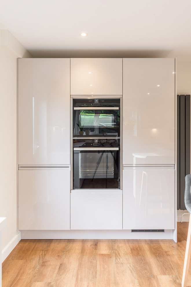 Photo of a medium sized contemporary u-shaped kitchen in Sussex with flat-panel cabinets, white cabinets, composite countertops, pink splashback, glass sheet splashback, a breakfast bar and white worktops.