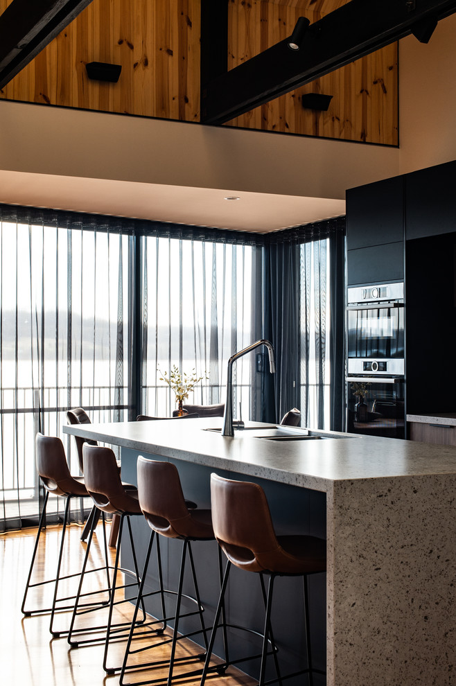 Contemporary galley kitchen in Other with a submerged sink, flat-panel cabinets, black cabinets, stainless steel appliances, medium hardwood flooring, an island, brown floors and grey worktops.