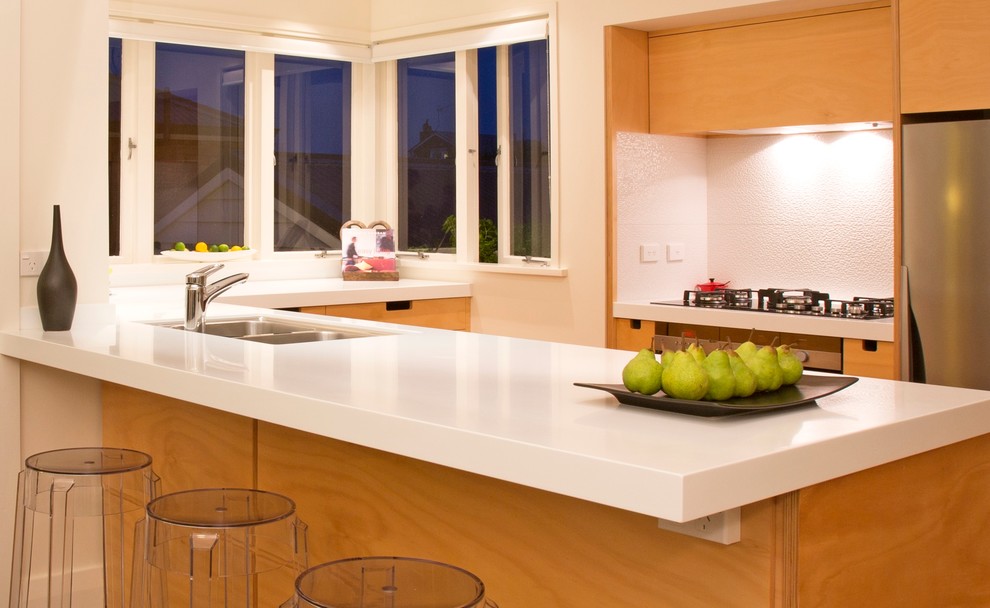 Kleine Moderne Wohnküche in U-Form mit Doppelwaschbecken, flächenbündigen Schrankfronten, hellen Holzschränken, Küchenrückwand in Weiß, Rückwand aus Keramikfliesen, Küchengeräten aus Edelstahl und braunem Holzboden in Auckland