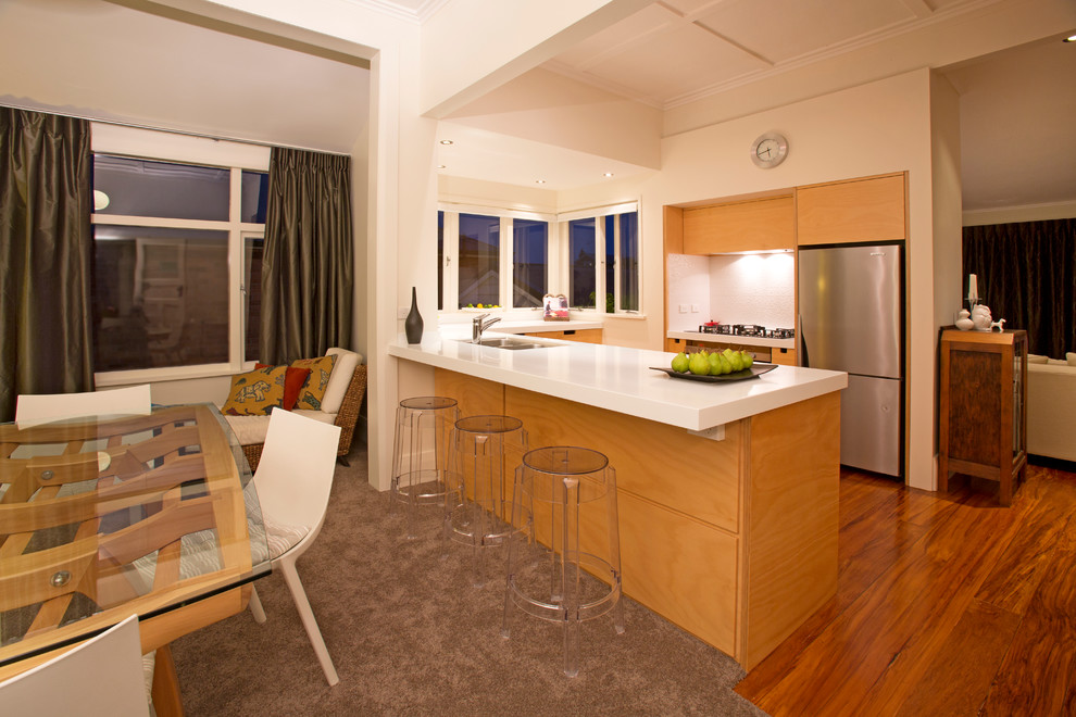 Kleine Moderne Wohnküche in U-Form mit flächenbündigen Schrankfronten, hellen Holzschränken, Doppelwaschbecken, Küchenrückwand in Weiß, Rückwand aus Keramikfliesen, Küchengeräten aus Edelstahl und braunem Holzboden in Auckland