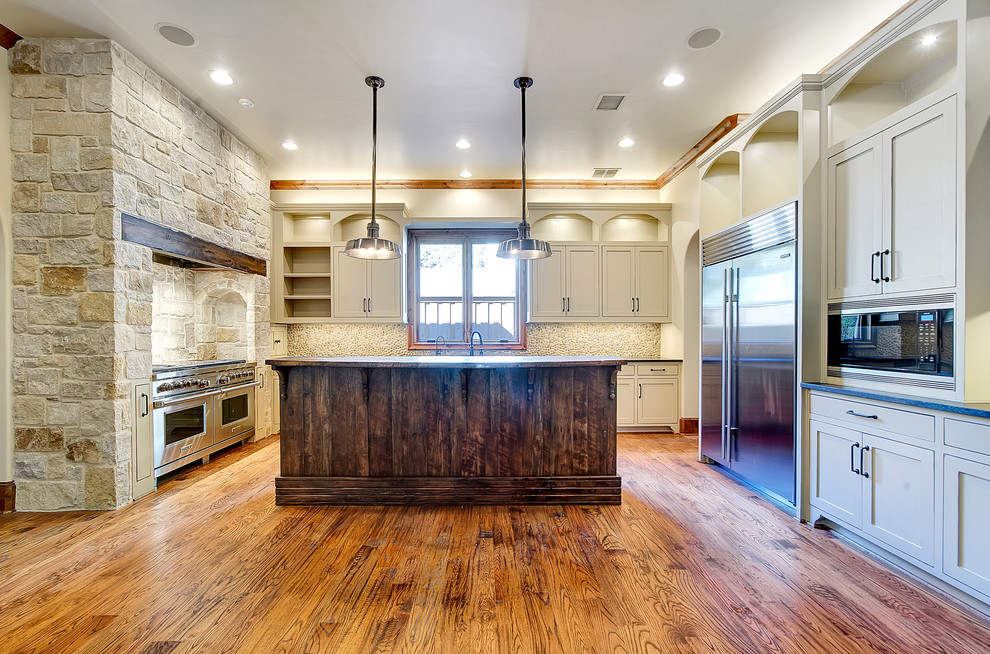 Mountain style l-shaped medium tone wood floor eat-in kitchen photo in Dallas with an undermount sink, distressed cabinets, granite countertops, multicolored backsplash, stainless steel appliances, shaker cabinets, stone tile backsplash and an island