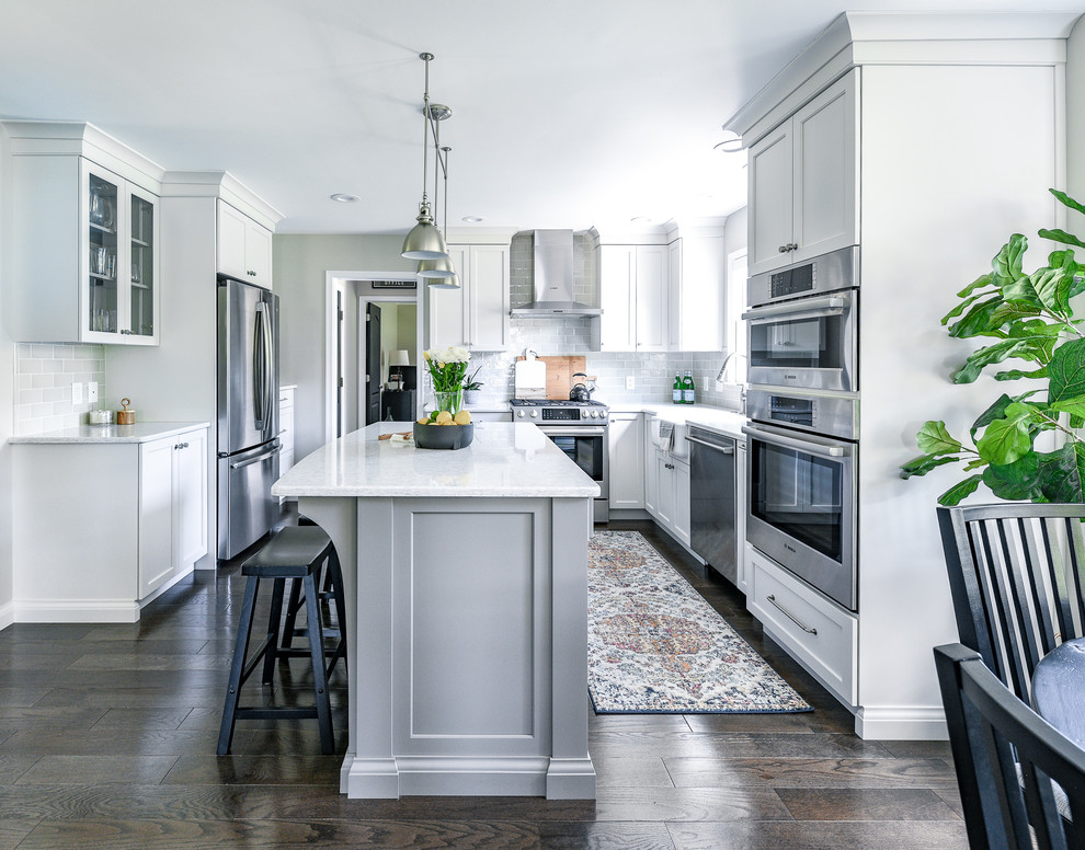 Klassisk inredning av ett mellanstort vit vitt kök, med en rustik diskho, luckor med infälld panel, grå skåp, bänkskiva i kvarts, grått stänkskydd, stänkskydd i keramik, rostfria vitvaror, mörkt trägolv och en köksö