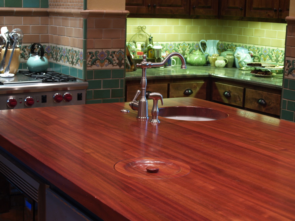 Diseño de cocina comedor ecléctica grande con fregadero bajoencimera, armarios con paneles con relieve, puertas de armario azules, encimera de madera, salpicadero gris, electrodomésticos de acero inoxidable, suelo de baldosas de cerámica y una isla