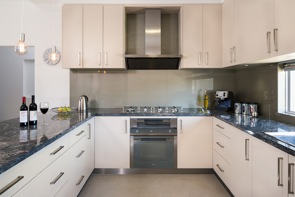 Bild på ett litet funkis u-kök, med släta luckor, beige skåp, marmorbänkskiva, grått stänkskydd, glaspanel som stänkskydd, rostfria vitvaror, klinkergolv i porslin och en halv köksö